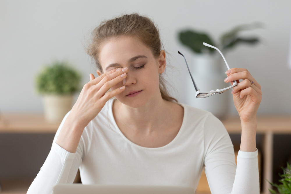 Woman with digital eye strain rubs her eyes and looks exhausted after hours at the computer