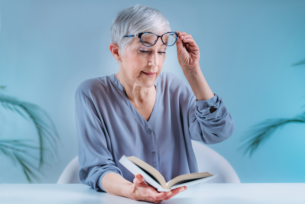 Woman in her 70s squints at a book and thinks about cataract surgery in Toronto